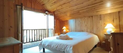 A wooden-paneled bedroom with a bed, bedside lamps, and a view through an open door.