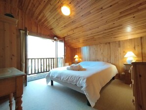 Ein Schlafzimmer mit Holzwandverkleidung, einem Bett, Nachttischlampen und Blick durch eine offene Tür.