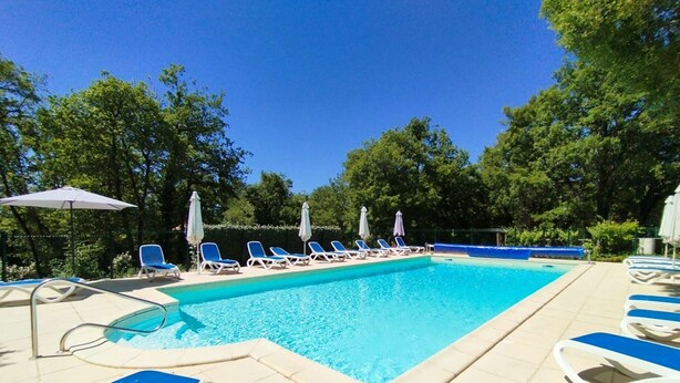 Een rechthoekig zwembad met blauw water, omringd door ligbedden en parasols.