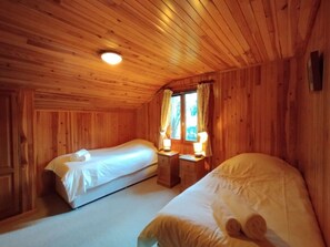 Een houten kamer met twee bedden, een raam met gordijnen en een kleine tafel met een lamp.