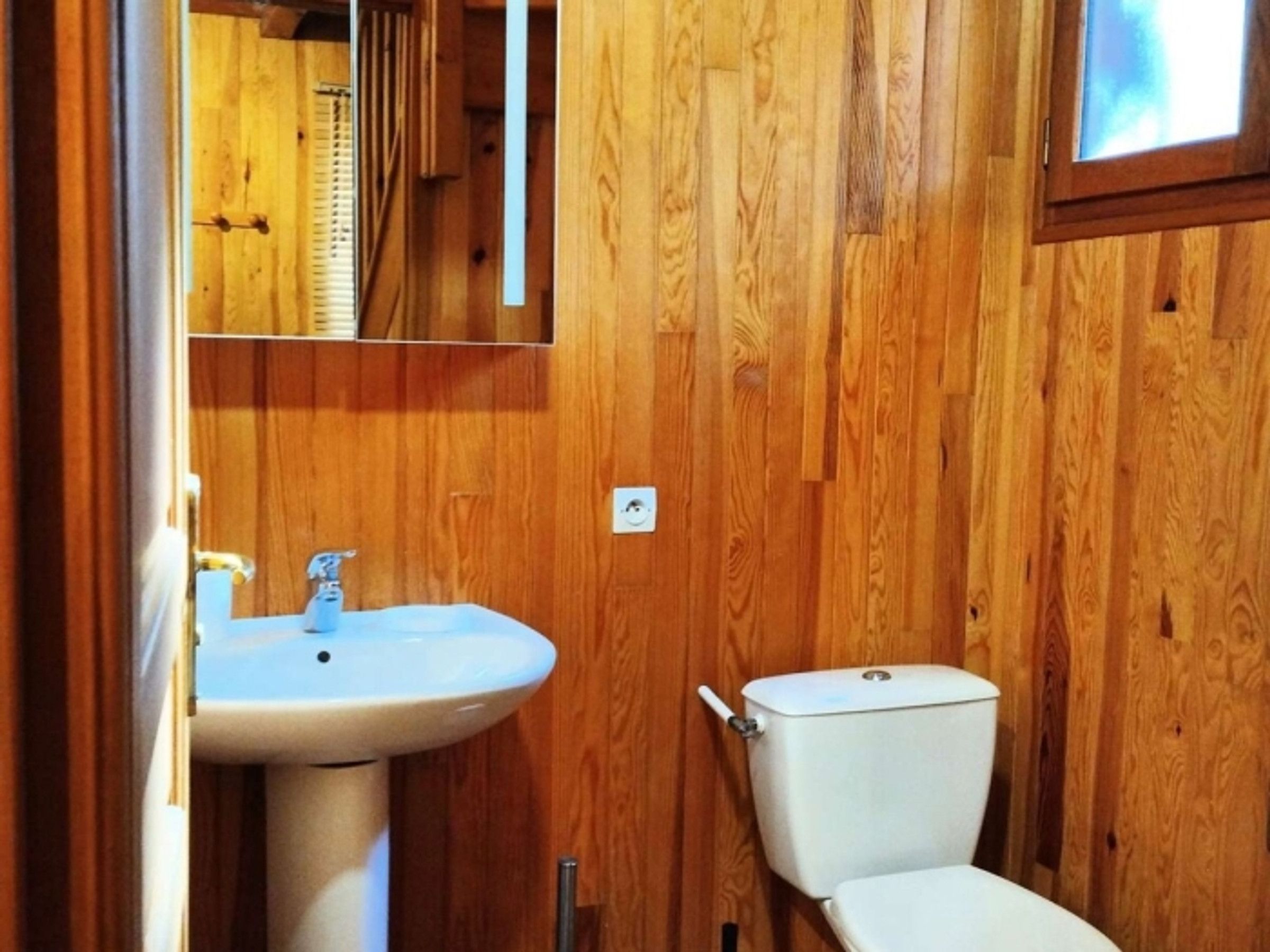 Een badkamer met houten lambrisering, een witte wastafel en een toilet.