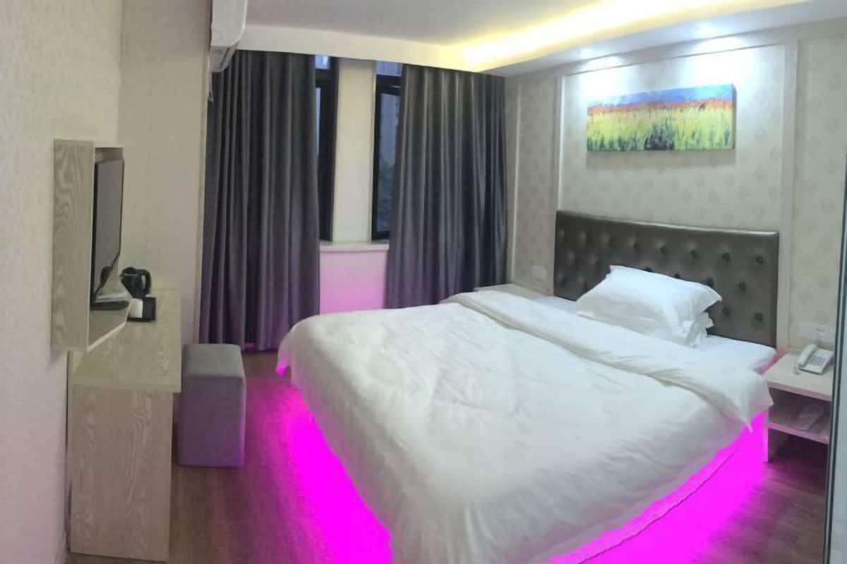 Ein Hotelzimmer mit einem großen Bett, einem Nachttisch mit Telefon, einer kleinen Sitzecke und einem Fenster mit Vorhängen.