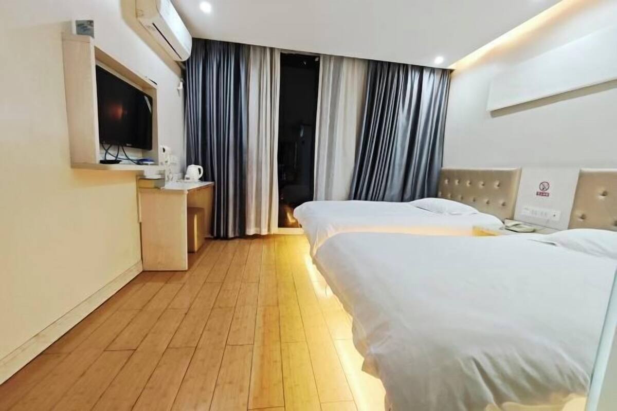 Ein Hotelzimmer mit zwei Betten, einem Fernseher, einem Schreibtisch mit Kaffeemaschine und einem Fenster mit Vorhängen.