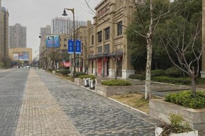 A city street with buildings, a sidewalk, and a road. - Yijia Hotel (Shanghai Jinshan New Town Wanda Plaza) (Shanghai)