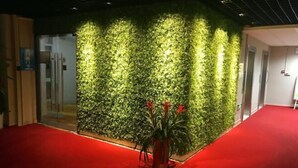 A reception area with a red carpet, a green vertical garden wall, and a potted plant with red flowers. - Yijia Hotel (Shanghai Jinshan New Town Wanda Plaza) (Shanghai)