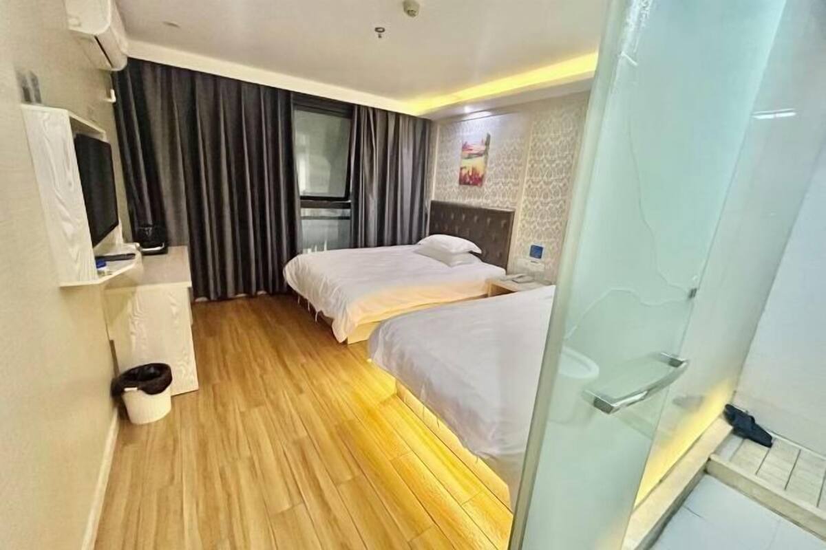 Ein Hotelzimmer mit zwei Betten, einem Fernseher, einem Fenster mit Vorhängen und einer Dusche.