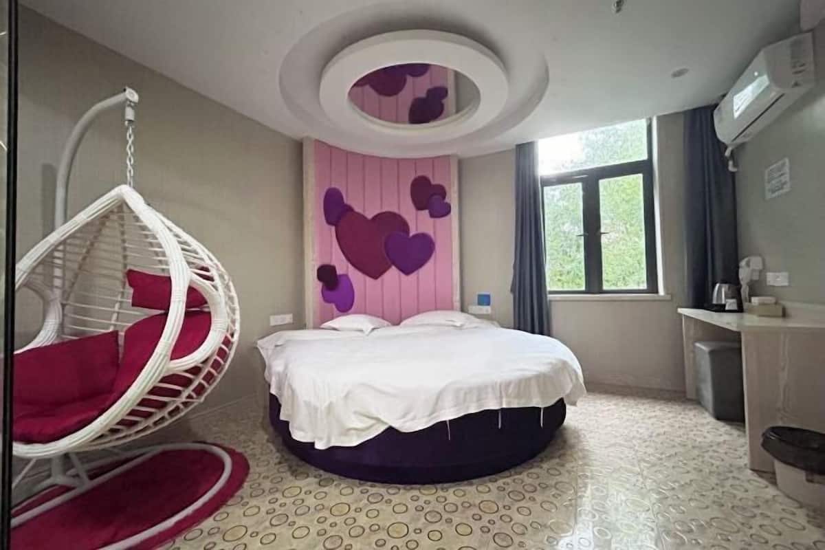 Ein Zimmer mit einem Bett, einem Hängestuhl, einem fenster mit Vorhängen und einer Wand mit Herzdekorationen.