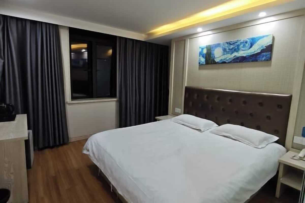 Ein Hotelzimmer mit Bett, Nachttisch, einem Bild und einem Fenster mit Vorhängen.