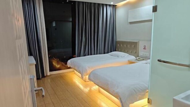 A hotel room with two beds, a sliding door to a balcony, and a white wall with a mounted air conditioner. - Yijia Hotel (Shanghai Jinshan New Town Wanda Plaza) (Shanghai)