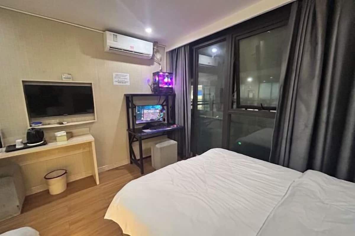 Ein Hotelzimmer mit Bett, Fernseher, Schreibtisch mit Computer und Fenster mit Vorhängen.