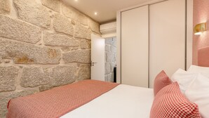 A bedroom with a stone wall, a bed with patterned bedding, and a wardrobe. - Charming Riverview Apartment in Porto (Porto)