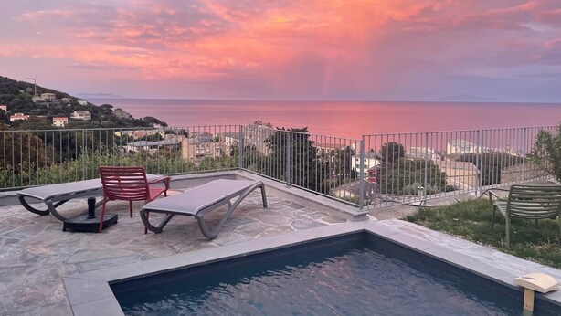 A rooftop pool with two lounge chairs and a table, overlooking a coastal town and the sea during sunset. - Air-conditioned villa with pool and panoramic sea view, 6 pax (Brando)
