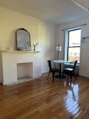 Une pièce avec une cheminée, une table à manger avec des chaises, une grande fenêtre et un radiateur.