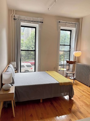 Una camera da letto con un letto, una sedia, un tavolo e due finestre con tende.
