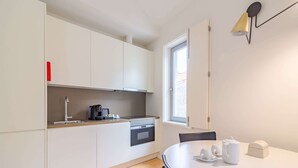 A modern kitchen with white cabinets, a built-in oven, a coffee maker, and a dining table with cups and a teapot. - Charming Central Escape, Oporto (Porto)