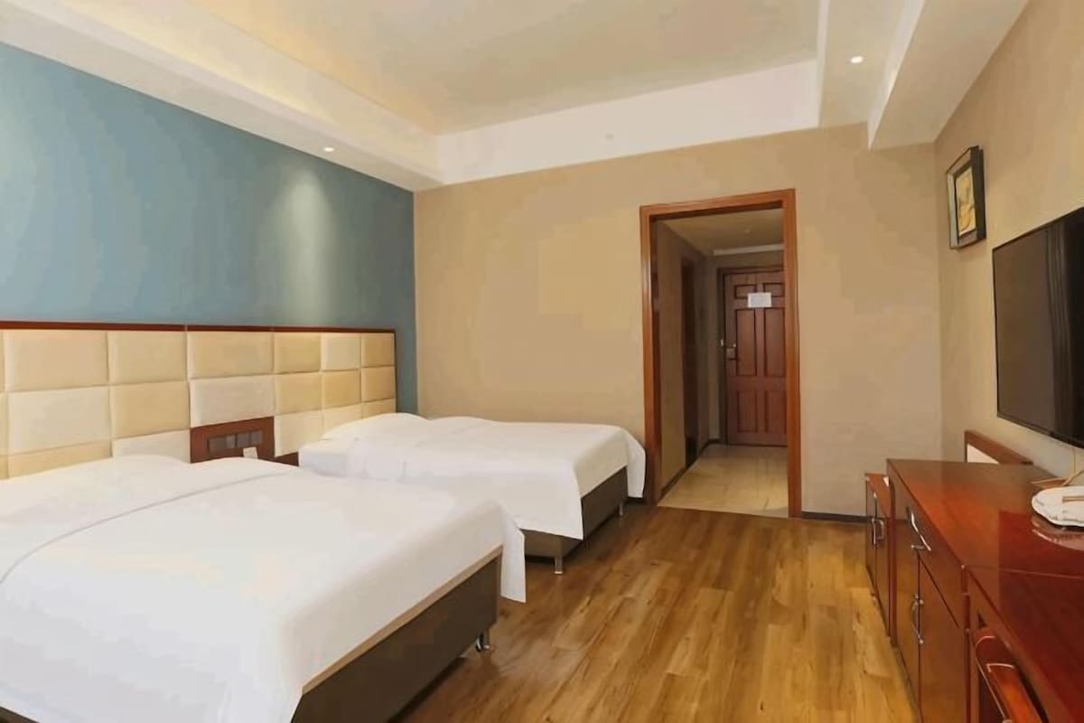 A hotel room with two beds, a wooden floor, a TV, and a door leading to another room.