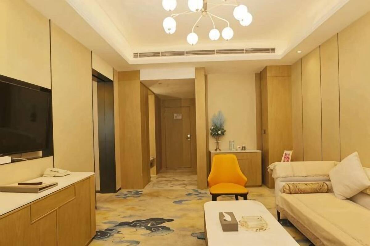Una camera d'albergo con televisore, un divano, una poltrona, una scrivania e pavimento tappezzato.