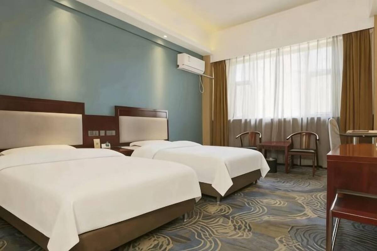 Una camera d'albergo con due letti, una scrivania, una sedia e una finestra con tende.