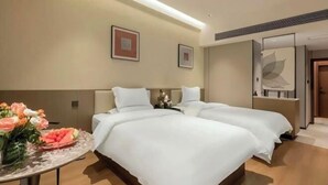 Une chambre d’hôtel avec deux lits, une petite table ornée de fleurs et un miroir.