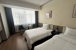 A hotel room with two beds, a small table, a chair, and a window with curtains.