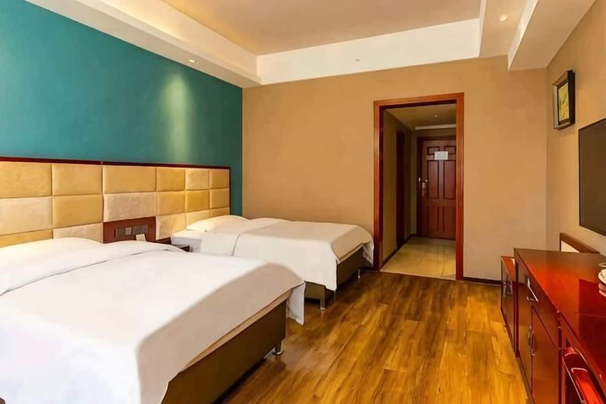 Una camera d'albergo con due letti, pavimento in legno, un armadietto rosso e un televisore.
