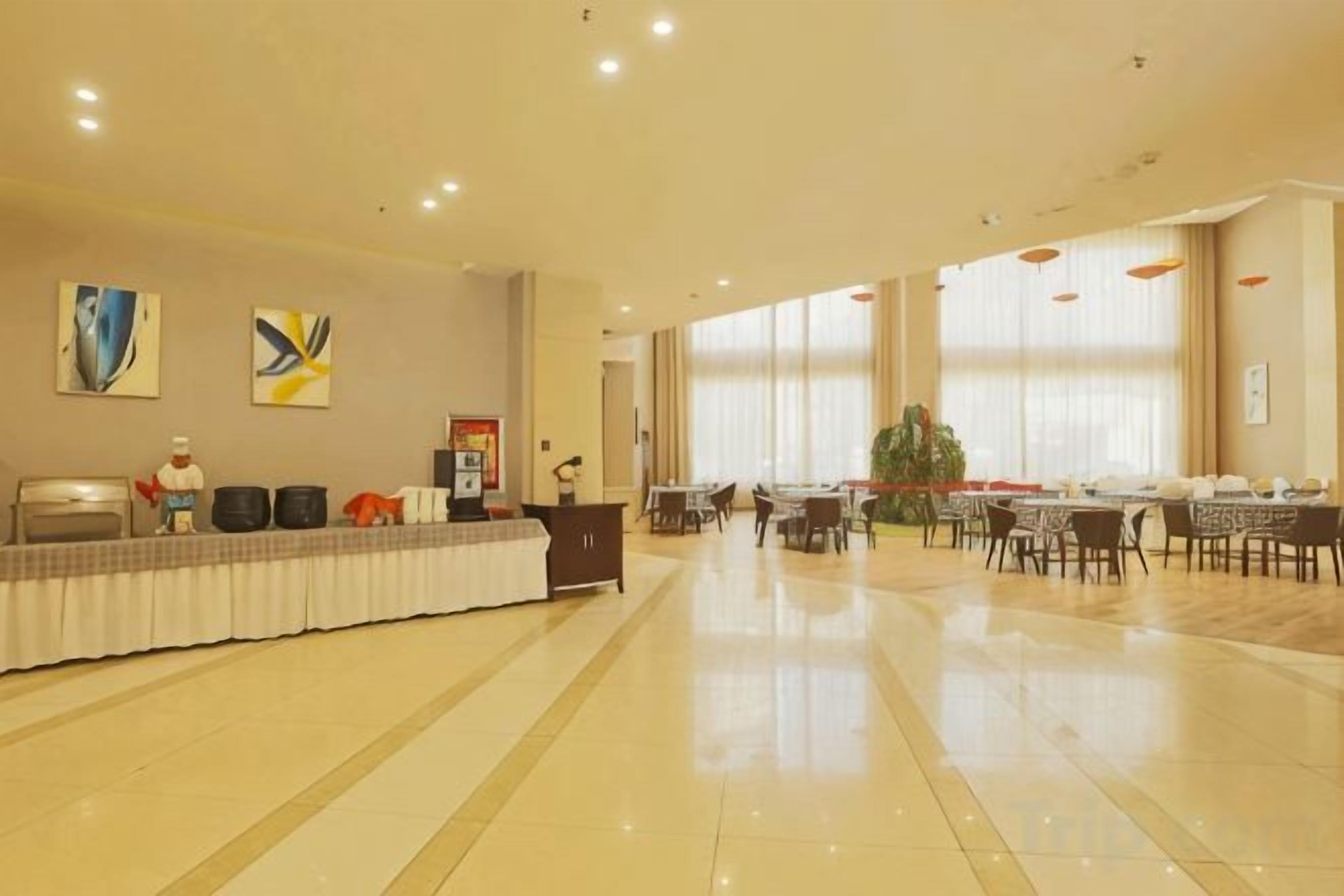 A spacious hotel lobby with a reception desk, dining area, and large windows.