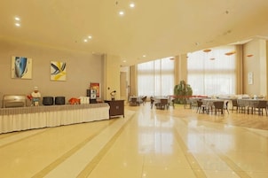 A spacious hotel lobby with a reception desk, dining area, and large windows.