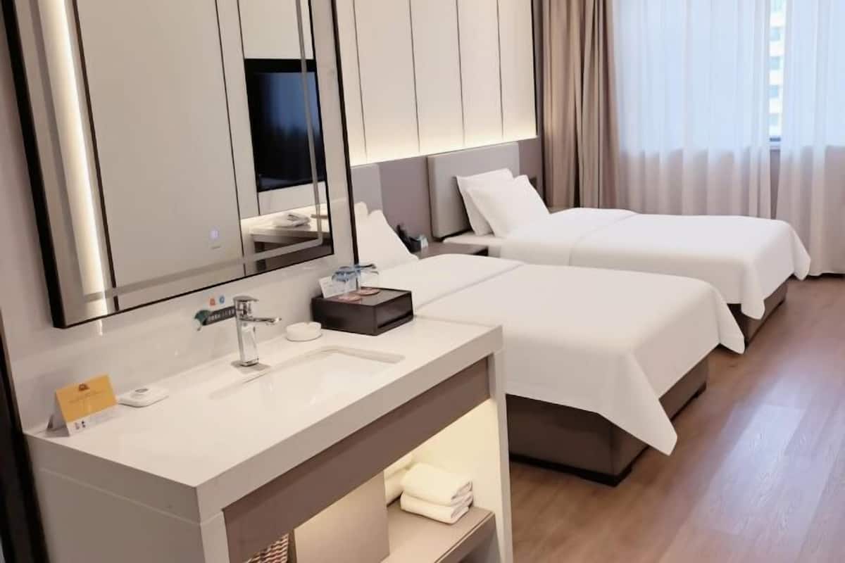 Camera d'albergo con due letti, un grande specchio, un moderno lavandino e un piccolo tavolo con articoli da toilette.
