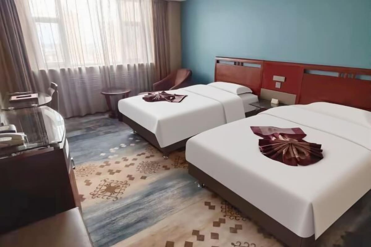 A hotel room with two beds, a desk, a chair, and a small table.