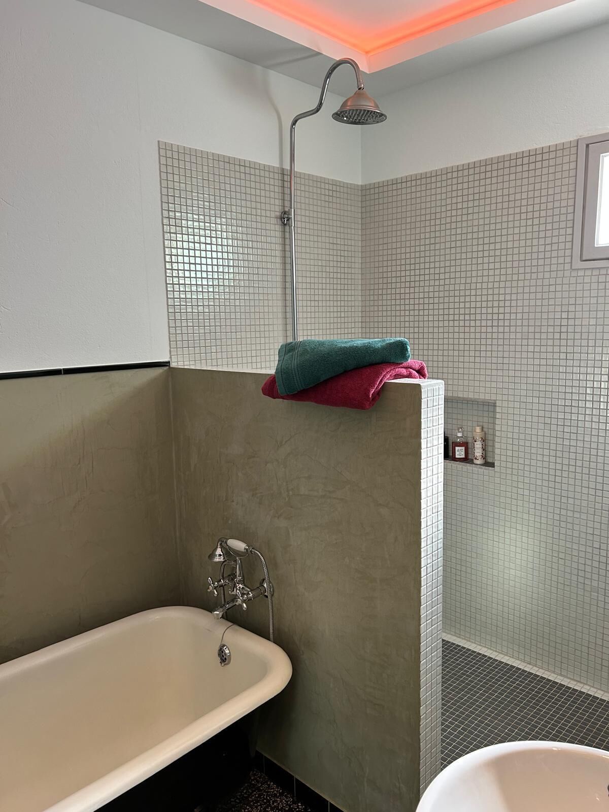 Een badkamer met een bad, een douche en betegelde wanden.