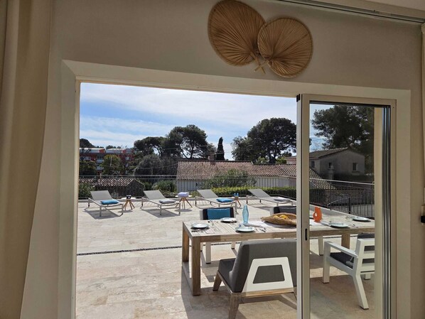 A modern outdoor patio with lounge chairs, a dining table, and a view of a residential area with trees and buildings.