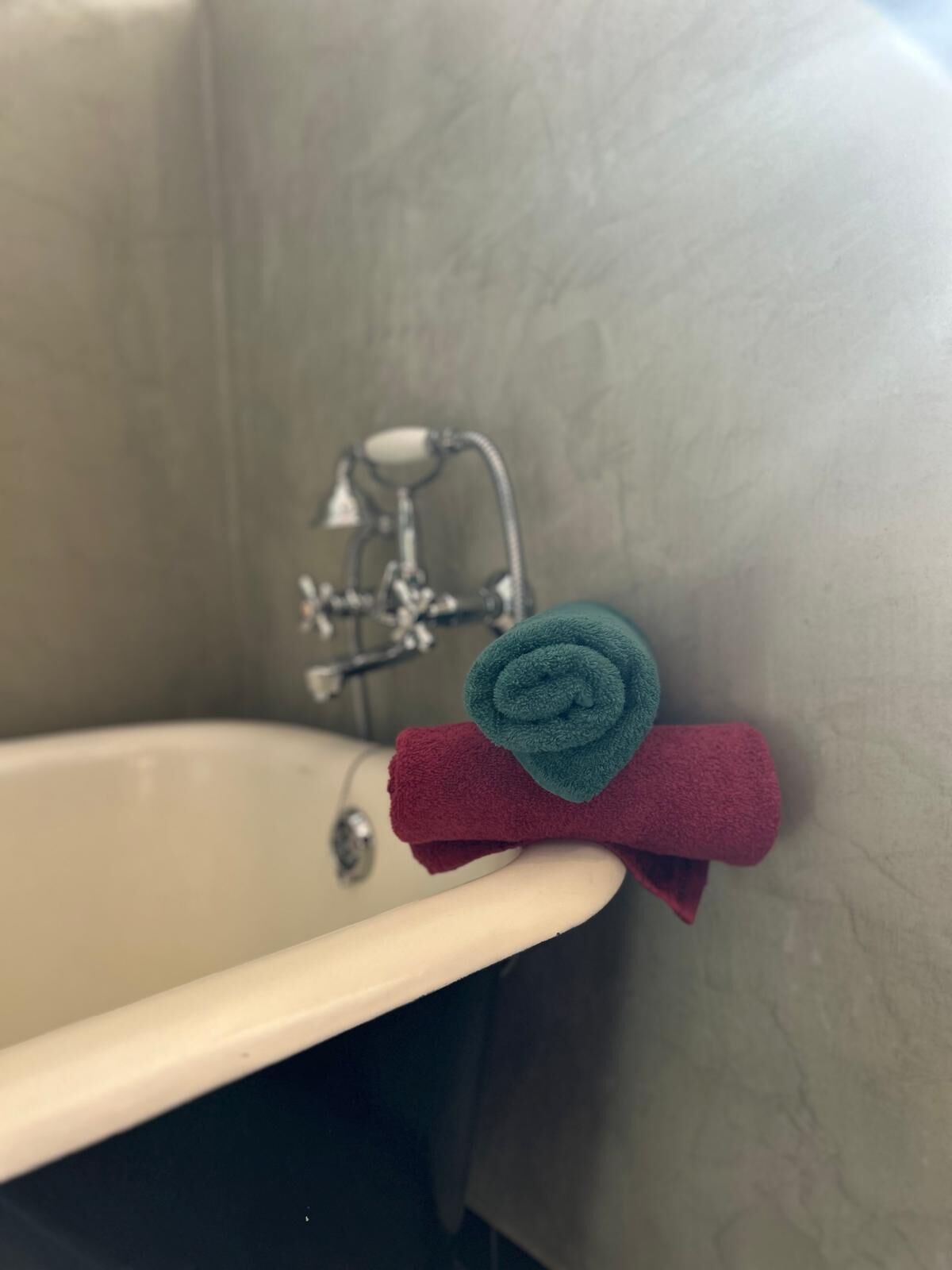 A bathtub with a towel rack holding two towels, one red and one teal.