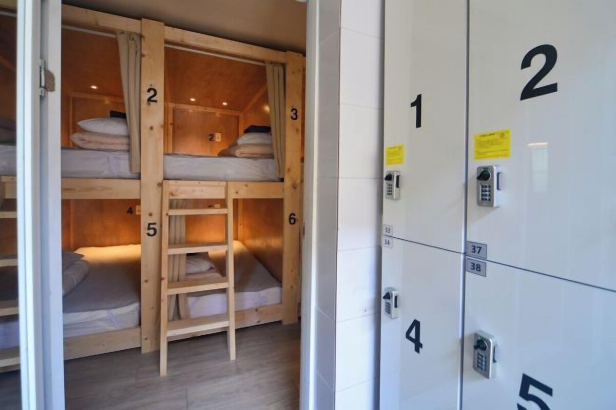 A dormitory-style room with bunk beds, numbered lockers, and a phone on the wall.