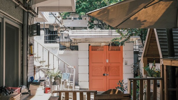 A courtyard with a wooden fence, a red door, and a staircase leading to a balcony. - Helloworld guesthouse (Seoul)