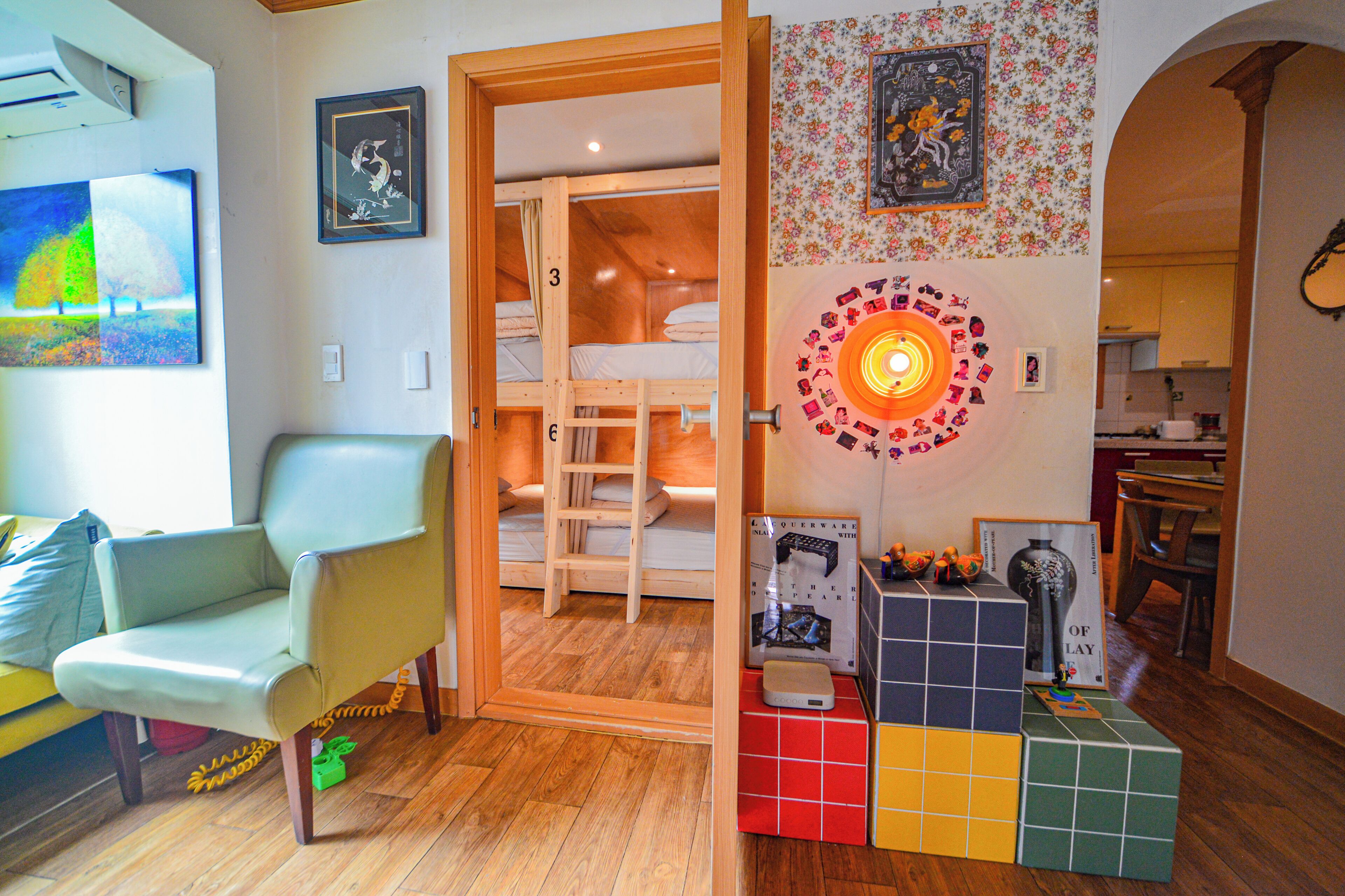 Une chambre avec un lit superposé, une chaise, une décoration murale colorée et une petite table sur laquelle se trouvent divers objets.