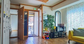 A room with a wooden floor, a yellow sofa, a mirror, a potted plant, and a door leading to a balcony. - Helloworld guesthouse (Seoul)