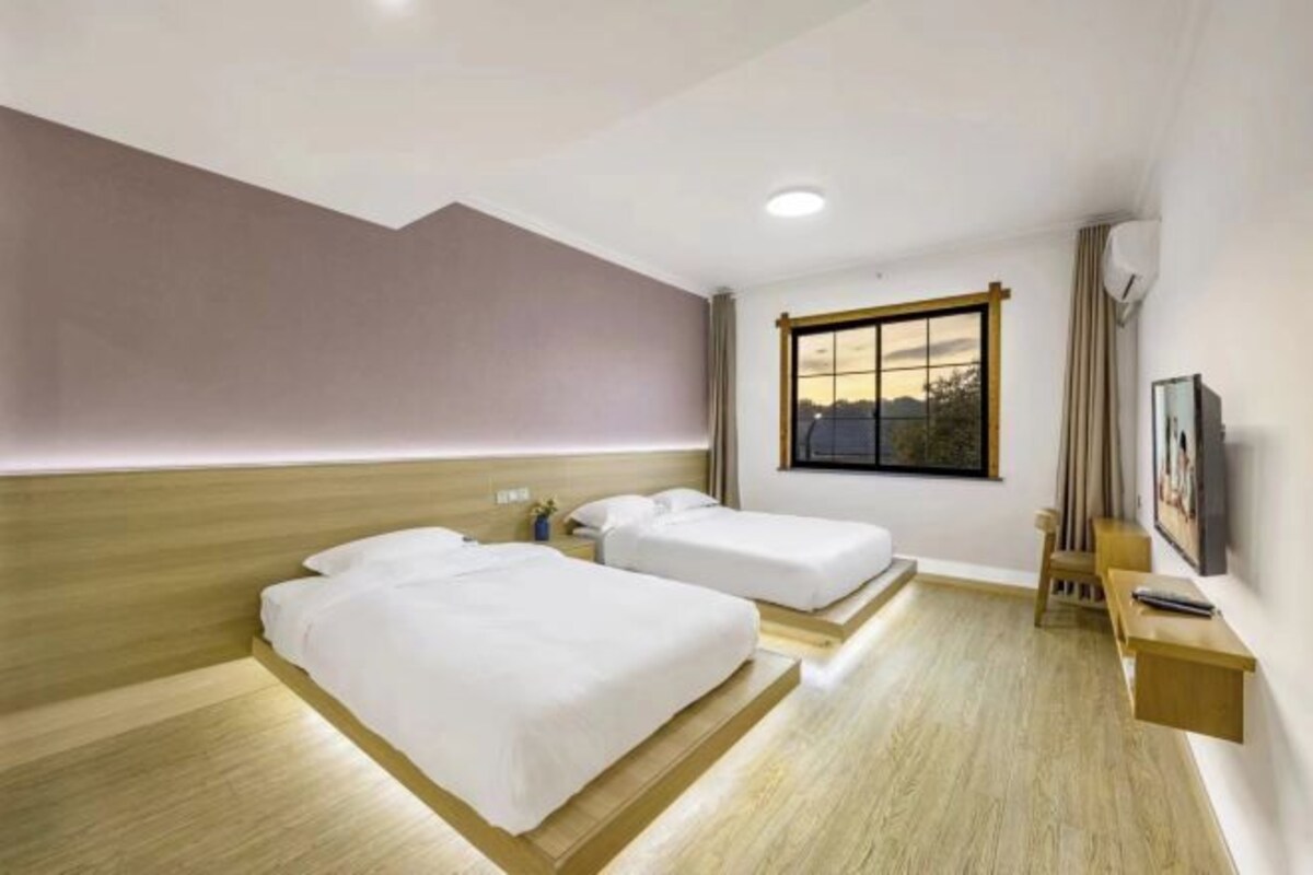 A hotel room with two beds, a window with a view, a desk, and a TV.