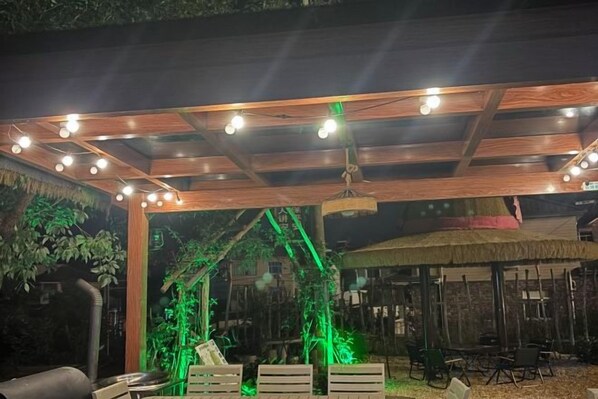 An outdoor area with a wooden pergola, string lights, and a thatched roof structure. - Anji Qile Farm (Anji)