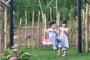 A child on a swing in a garden with a wooden fence and greenery in the background. - Anji Qile Farm (Anji)