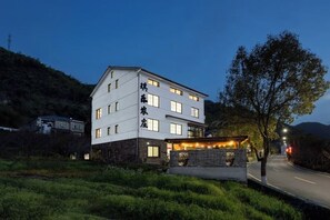 A multi-story hotel with a flat roof, a stone facade, and a well-lit entrance. - Anji Qile Farm (Anji)
