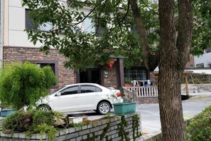 A white car parked in front of a building with a brick facade, a tree, and a small garden area. - Anji Qile Farm (Anji)