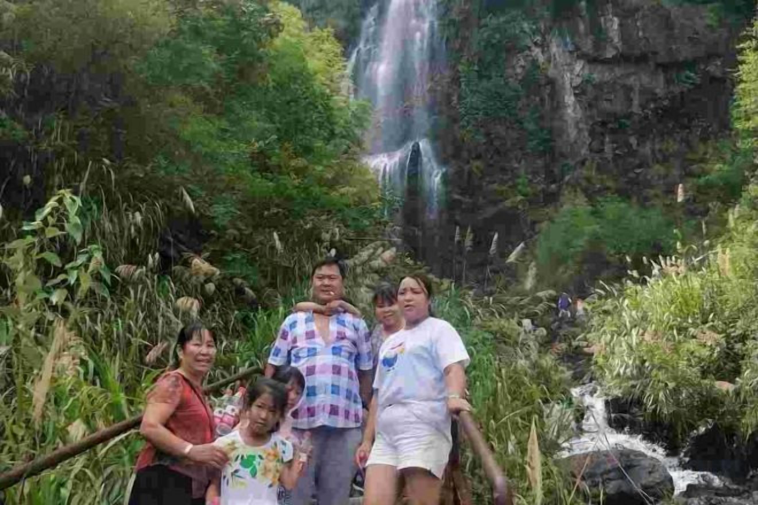 A group of people standing in a natural setting with a waterfall in the background.