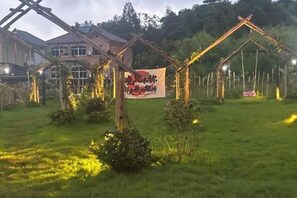 Een tuin met een houten boog, een schommel en een spandoek met tekst.