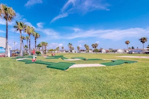 Un parcours de golf avec des fairways verdoyants, des bunkers de sable et un ciel bleu dégagé.