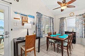 Un espace repas comprenant une table, des chaises, un ventilateur de plafond et une fenêtre avec des rideaux.