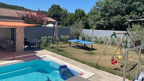 Ein Garten mit Swimmingpool, einer Terrasse mit Gartenmöbeln und einer Schaukel.