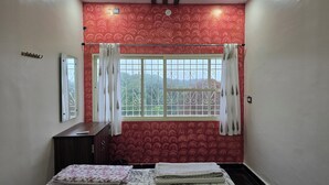A bedroom with a bed, a wardrobe, a window with curtains, and a mirror on the wall. - Lakshmi Villa (Hospet)