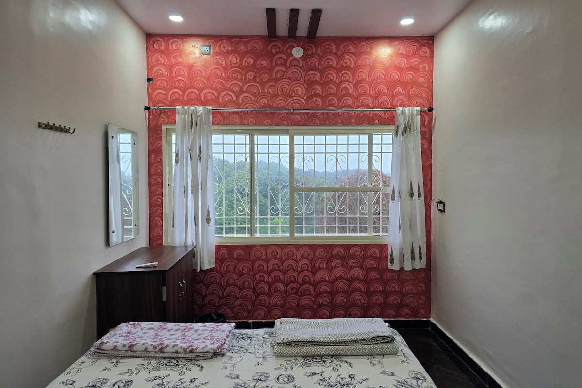 A bedroom with a bed, a wardrobe, a window with curtains, and a mirror on the wall.
