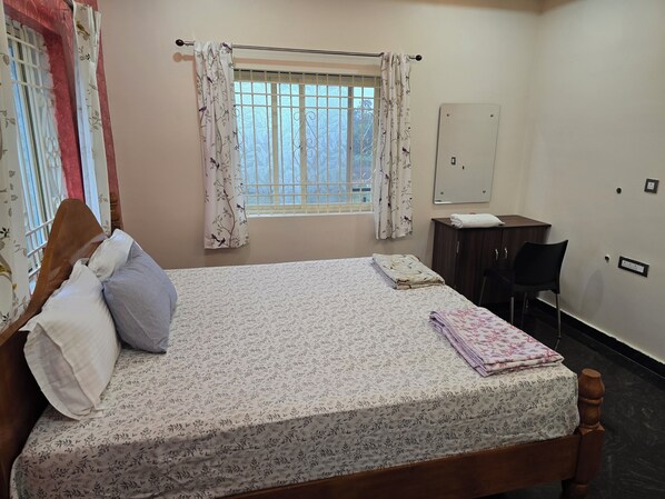 A neatly made bed with floral bedding, a wooden headboard, and a bedside table with a folded towel. - Lakshmi Villa (Hospet)