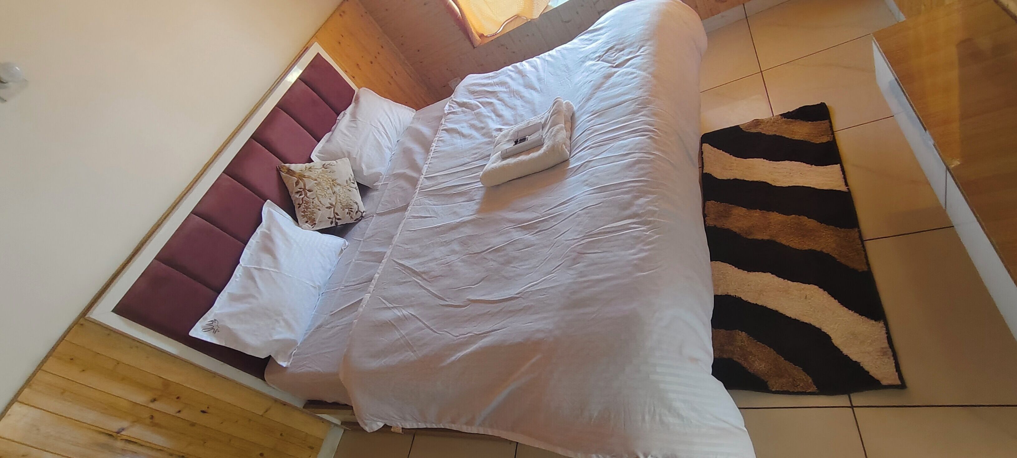 Ein Bett mit weißer Bettwäsche und einem roten Kopfteil, ein Teppich mit ZEBRA-MUSTER und Holzböden.